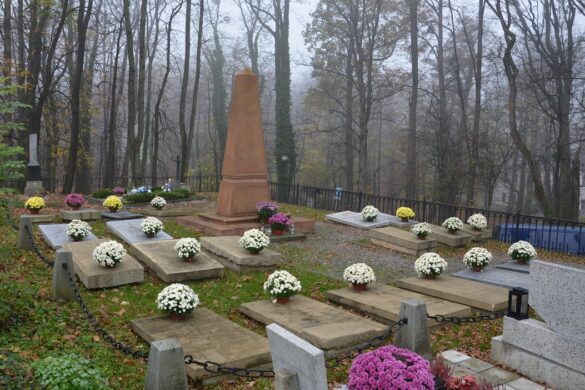 Po środku obelisk otoczony płaskimi płytami nagrobnymi na których znajdują się kwiaty