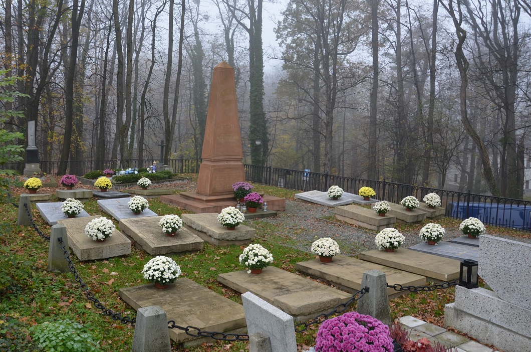Po środku obelisk otoczony płaskimi płytami nagrobnymi na których znajdują się kwiaty