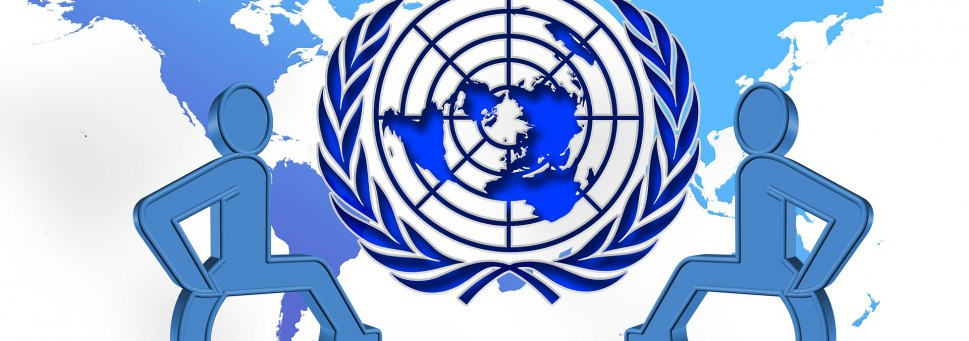 Dwa symbole osób niepełnosprawnych w tle logo ONZ- rzut kontynentów od strony bieguna pólnocnego w otoczeniu wieńca laurowego