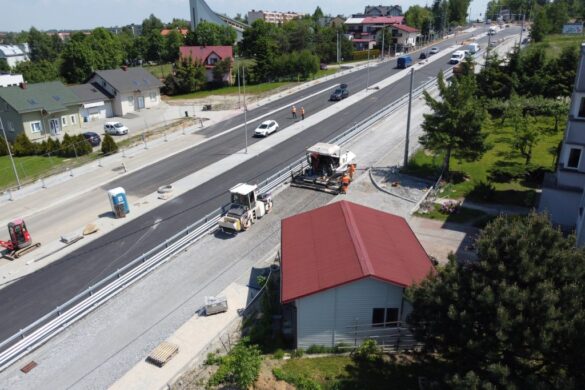 Widok z lotu ptaka na remontowaną dwujezdniową ulicę. Widoczne pojazdy budowlane oraz budynki wzdłuż ulicy.